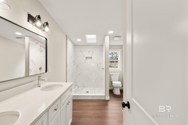 full bathroom with toilet, a sink, a marble finish shower, wood finished floors, and double vanity