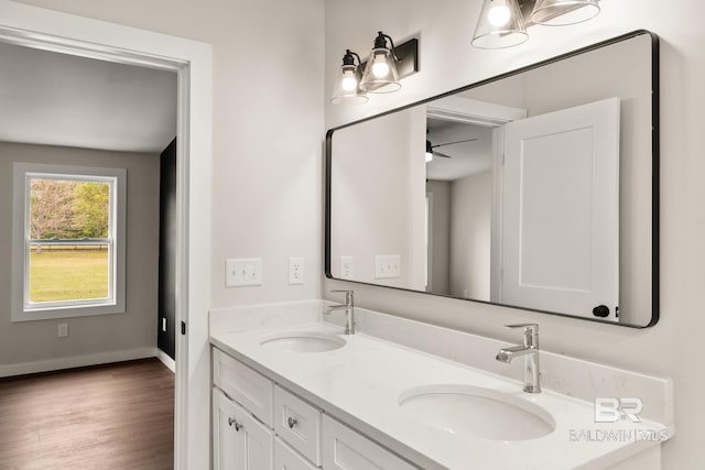full bathroom with baseboards, wood finished floors, double vanity, and a sink
