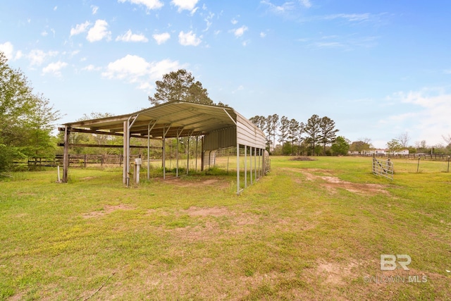 view of yard with driveway, an outbuilding, fence, a carport, and a rural view