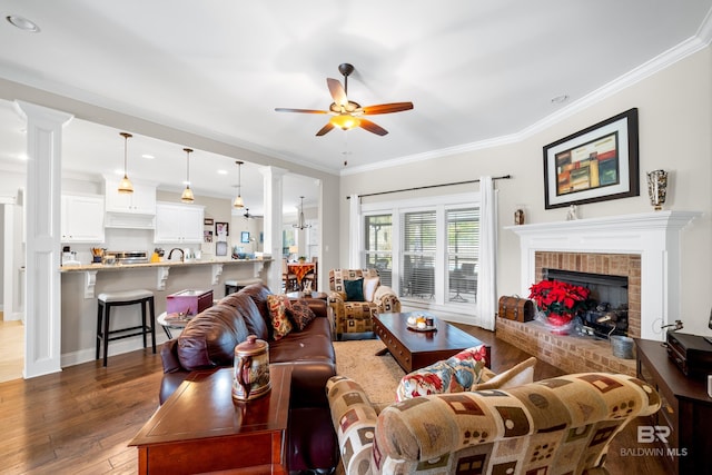 living room with ceiling fan, dark hardwood / wood-style flooring, ornamental molding, and a brick fireplace