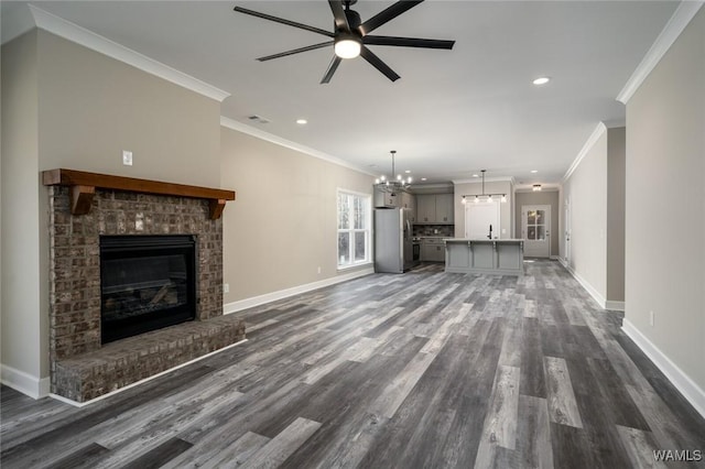 unfurnished living room featuring ceiling fan with notable chandelier, dark wood-type flooring, crown molding, sink, and a fireplace
