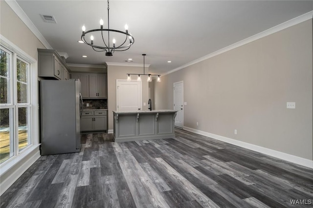 kitchen featuring stainless steel refrigerator, an island with sink, decorative light fixtures, gray cabinets, and ornamental molding