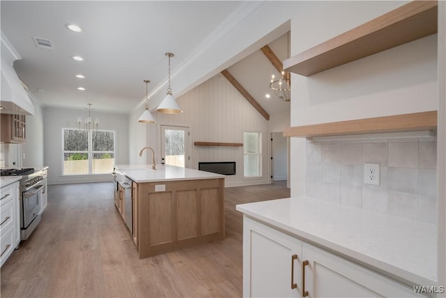 kitchen with stainless steel stove, lofted ceiling with beams, an island with sink, white cabinets, and a notable chandelier