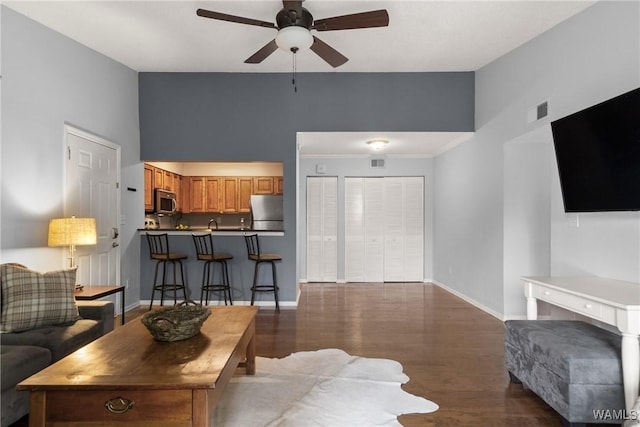 living room with ceiling fan, visible vents, wood finished floors, baseboards, and a high ceiling