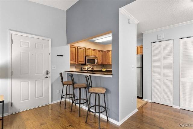 kitchen featuring brown cabinets, dark countertops, appliances with stainless steel finishes, wood finished floors, and a kitchen bar