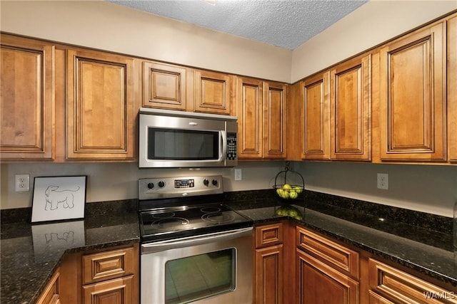 kitchen with brown cabinets, stainless steel appliances, a textured ceiling, and dark stone countertops