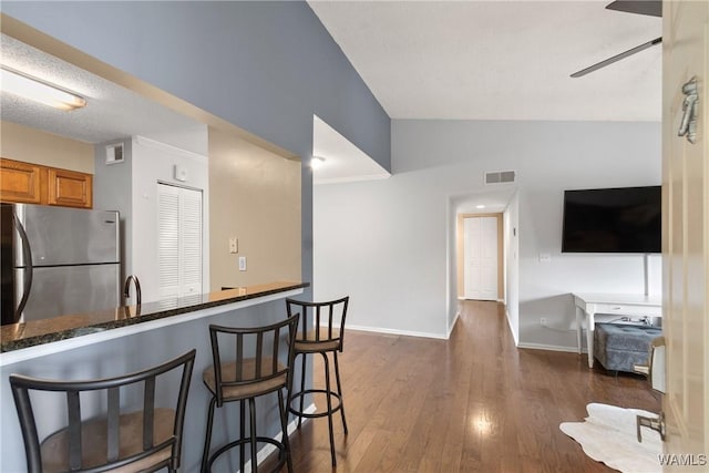kitchen with brown cabinetry, freestanding refrigerator, baseboards, lofted ceiling, and visible vents
