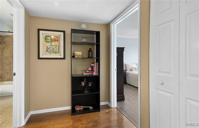 hall featuring a textured ceiling, baseboards, and wood finished floors