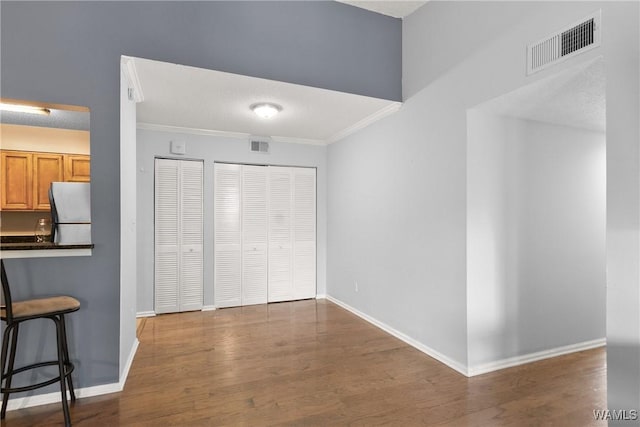 unfurnished dining area featuring baseboards, ornamental molding, wood finished floors, and visible vents