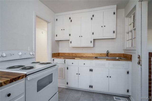 kitchen with sink, light tile patterned floors, butcher block countertops, white electric range oven, and white cabinetry