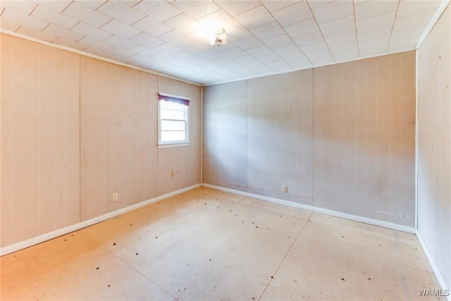 spare room with wooden walls, baseboards, and concrete floors