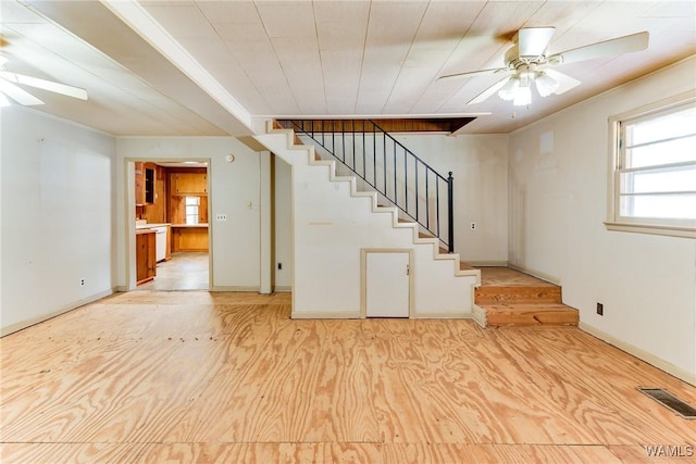 below grade area with crown molding, a ceiling fan, wood finished floors, visible vents, and stairway
