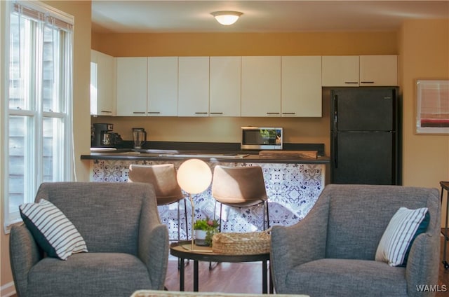 kitchen featuring dark countertops, white cabinetry, stainless steel microwave, and freestanding refrigerator