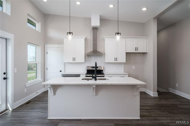 kitchen featuring white cabinetry, an island with sink, pendant lighting, and wall chimney range hood