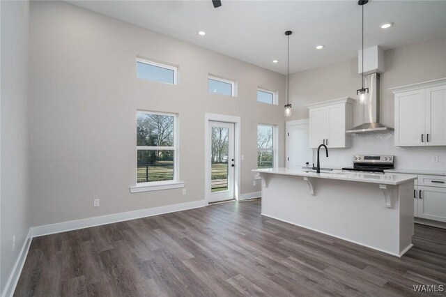 kitchen featuring pendant lighting, white cabinetry, electric stove, a kitchen island with sink, and wall chimney range hood