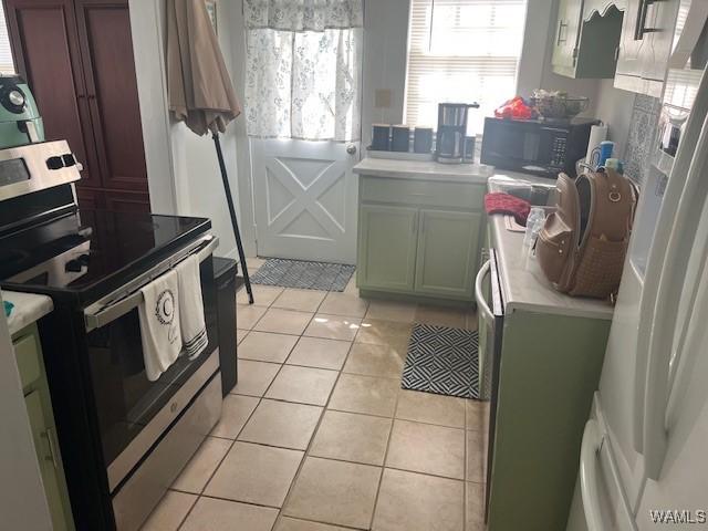 kitchen featuring stainless steel range with electric cooktop, black microwave, light countertops, freestanding refrigerator, and light tile patterned floors
