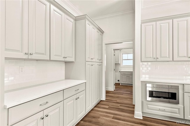 kitchen featuring white cabinetry, stainless steel microwave, dark wood-type flooring, crown molding, and decorative backsplash