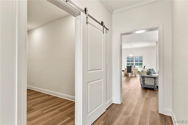 corridor with hardwood / wood-style floors, a barn door, crown molding, and an inviting chandelier