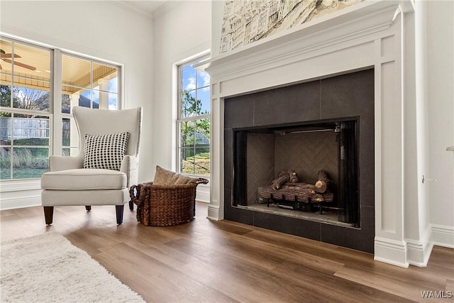 living area with wood-type flooring, crown molding, and a tiled fireplace