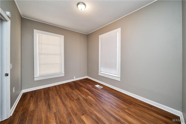 empty room with baseboards, visible vents, ornamental molding, and dark wood-type flooring