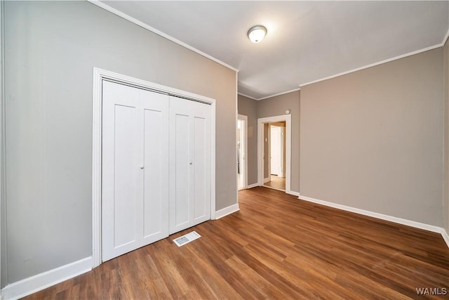 unfurnished bedroom with visible vents, crown molding, a closet, wood finished floors, and baseboards