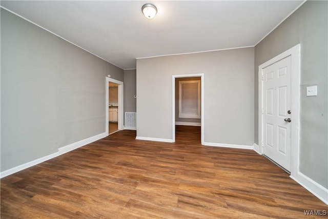 empty room with crown molding, baseboards, wood finished floors, and visible vents