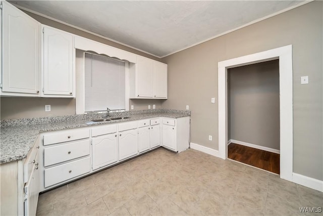 kitchen featuring white cabinetry, baseboards, ornamental molding, and a sink