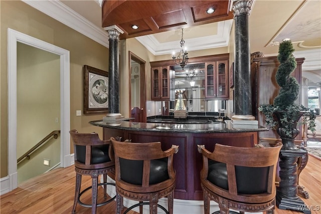 bar with light wood-type flooring, ornate columns, ornamental molding, coffered ceiling, and hanging light fixtures