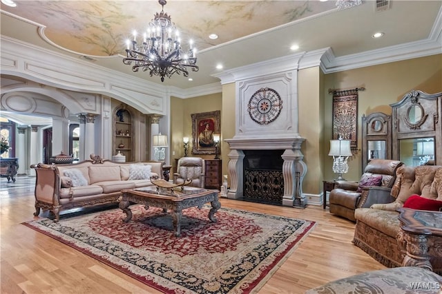 living room with a large fireplace, an inviting chandelier, light hardwood / wood-style flooring, and crown molding