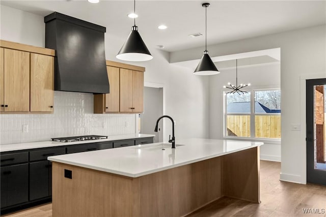 kitchen with sink, decorative light fixtures, a kitchen island with sink, and custom exhaust hood