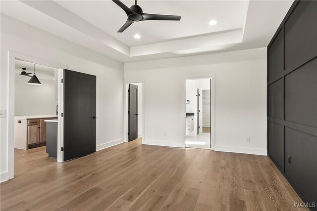 unfurnished bedroom featuring a raised ceiling, ceiling fan, connected bathroom, and light hardwood / wood-style floors