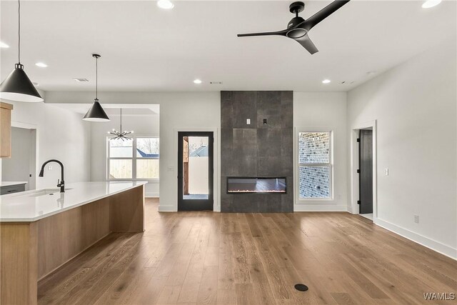 kitchen with sink, hanging light fixtures, a fireplace, an island with sink, and light wood-type flooring