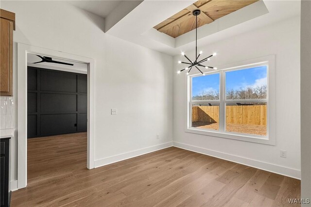 unfurnished dining area with a raised ceiling, hardwood / wood-style floors, and an inviting chandelier