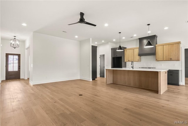 kitchen featuring ceiling fan with notable chandelier, decorative backsplash, a center island with sink, decorative light fixtures, and light wood-type flooring