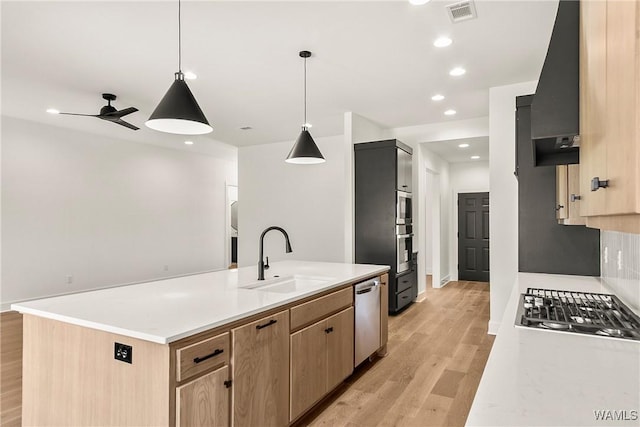 kitchen featuring sink, hanging light fixtures, a center island with sink, light hardwood / wood-style flooring, and appliances with stainless steel finishes