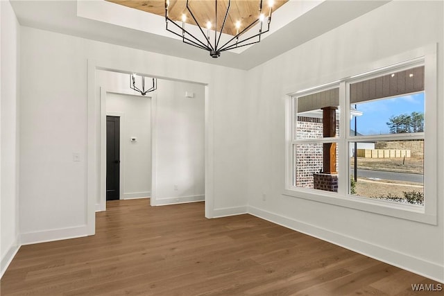 empty room featuring wood-type flooring and a notable chandelier