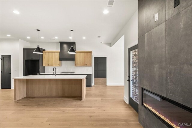 kitchen with pendant lighting, an island with sink, light hardwood / wood-style floors, gas stovetop, and wall chimney range hood