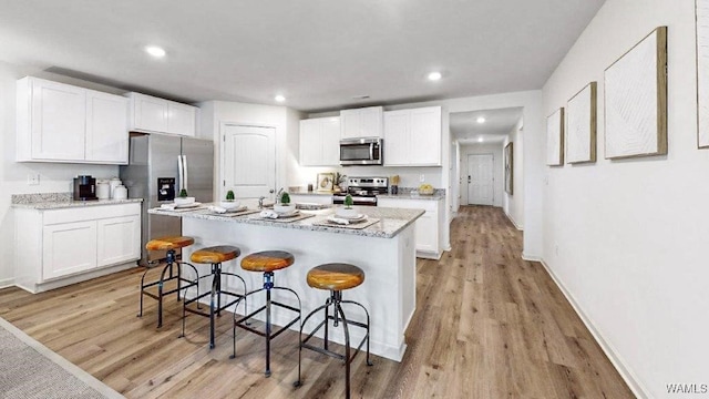 kitchen featuring white cabinets, stainless steel appliances, a kitchen island with sink, and light hardwood / wood-style flooring