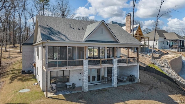 rear view of house featuring a patio area, a lawn, roof with shingles, and a sunroom