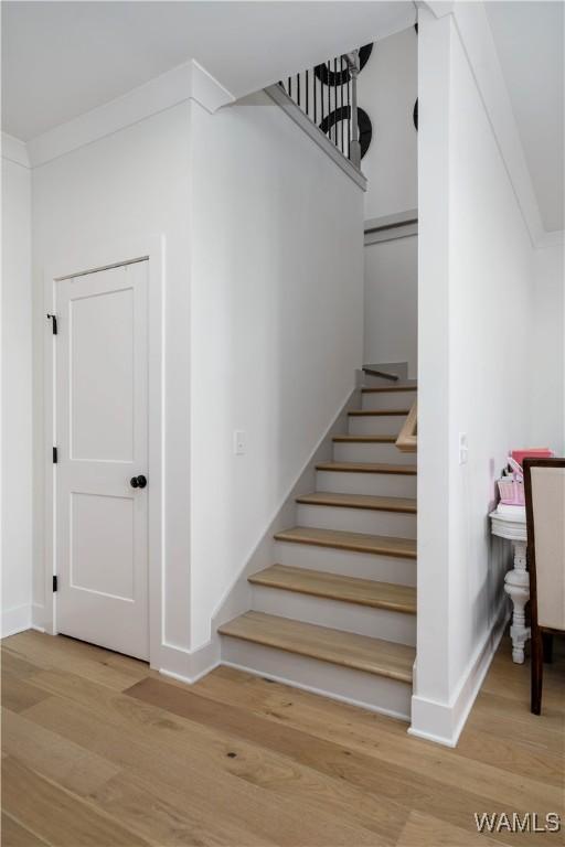 stairs with wood finished floors, baseboards, and ornamental molding