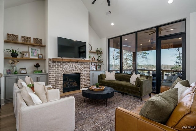 living area with a brick fireplace, high vaulted ceiling, a ceiling fan, and wood finished floors