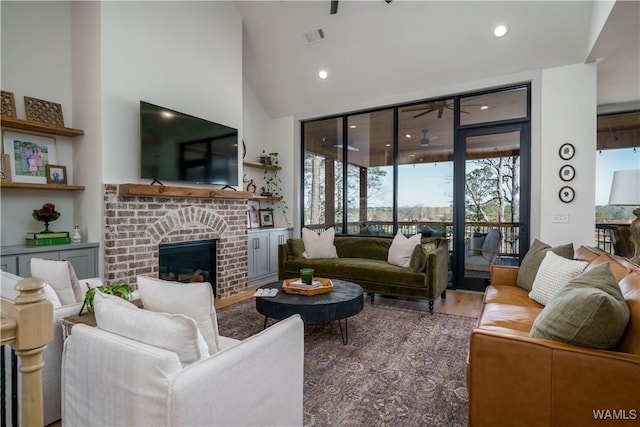 living area featuring a ceiling fan, wood finished floors, visible vents, a high ceiling, and a brick fireplace