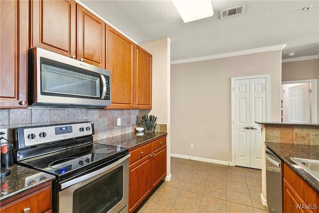 kitchen featuring dark stone countertops, light tile patterned floors, ornamental molding, and appliances with stainless steel finishes