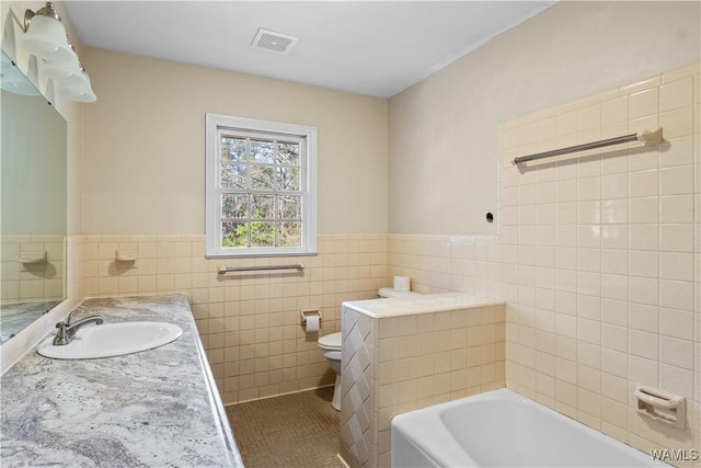 bathroom featuring tile walls, a tub to relax in, vanity, toilet, and tile patterned floors