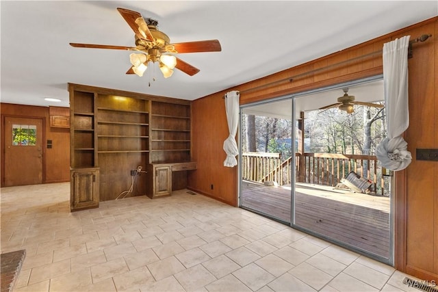 interior space with light tile patterned flooring, ceiling fan, built in desk, and wood walls