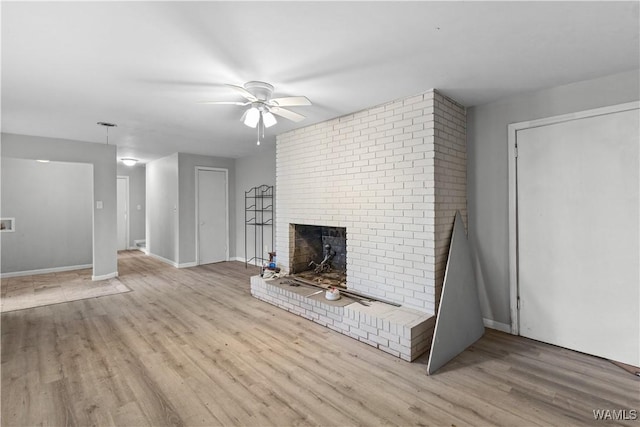 unfurnished living room with ceiling fan, a brick fireplace, and light wood-type flooring