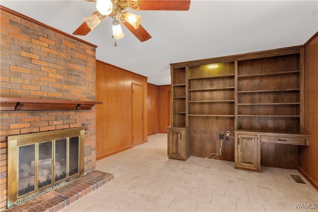 unfurnished living room with ceiling fan, a brick fireplace, and wood walls