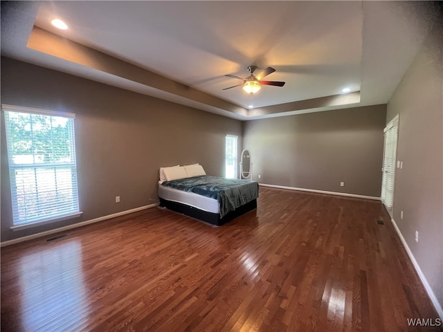 unfurnished bedroom featuring dark hardwood / wood-style floors, a raised ceiling, and ceiling fan