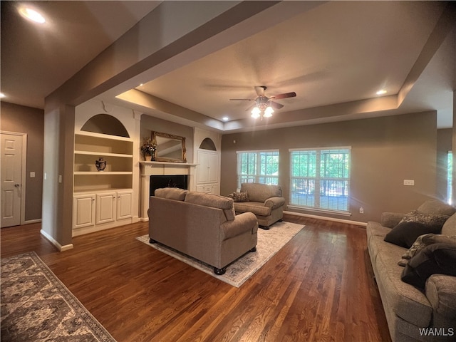 living room with a tray ceiling, ceiling fan, dark hardwood / wood-style flooring, and built in features