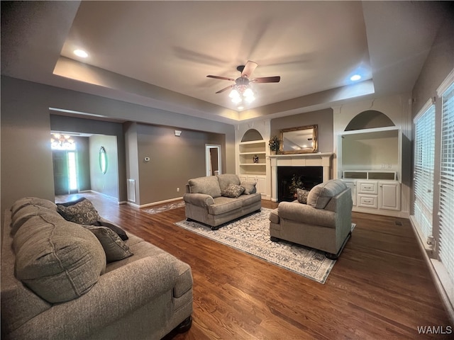 living room featuring a raised ceiling, ceiling fan, dark hardwood / wood-style flooring, and built in features